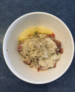 Raw Ground beef, chopped onion, eggs, breadcrumbs and spices in a bowl