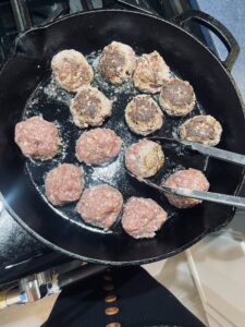 Meatballs frying in a cast iron skillet