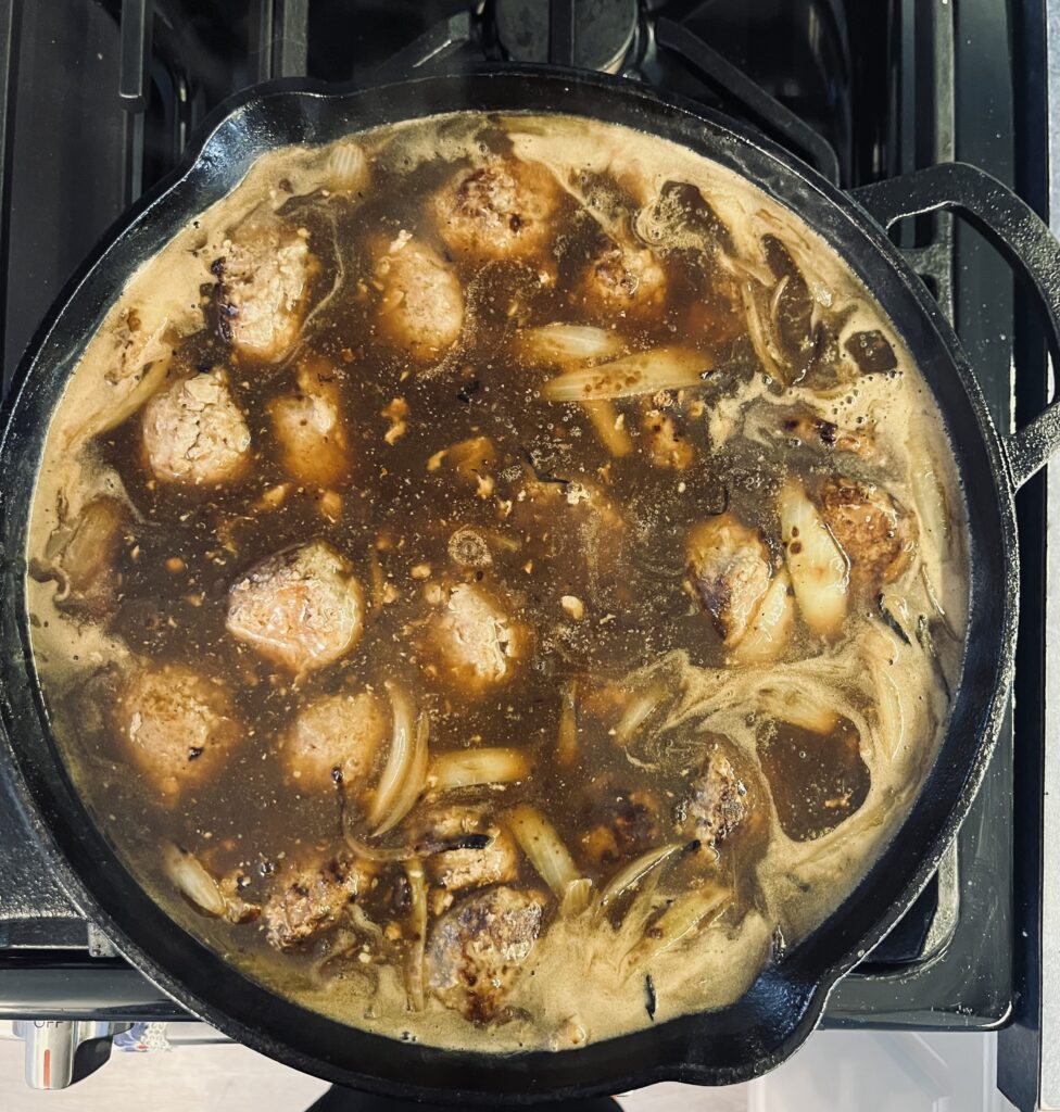 Savoury meatballs with gravy cooking in a cast iron pan